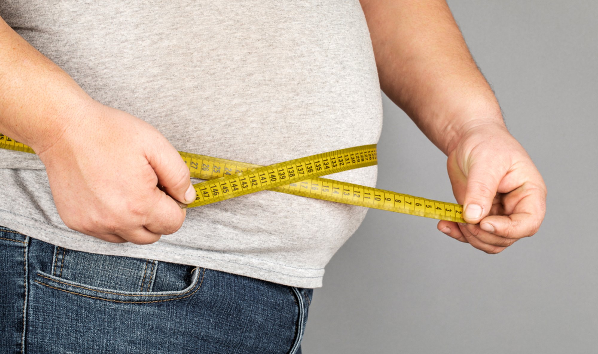 Person measuring waist circumference with a yellow tape measure.